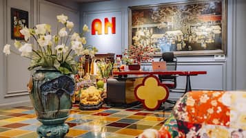 A room with a checkered floor, a large vase with flowers, a Buddha statue, and a painting on the wall.
