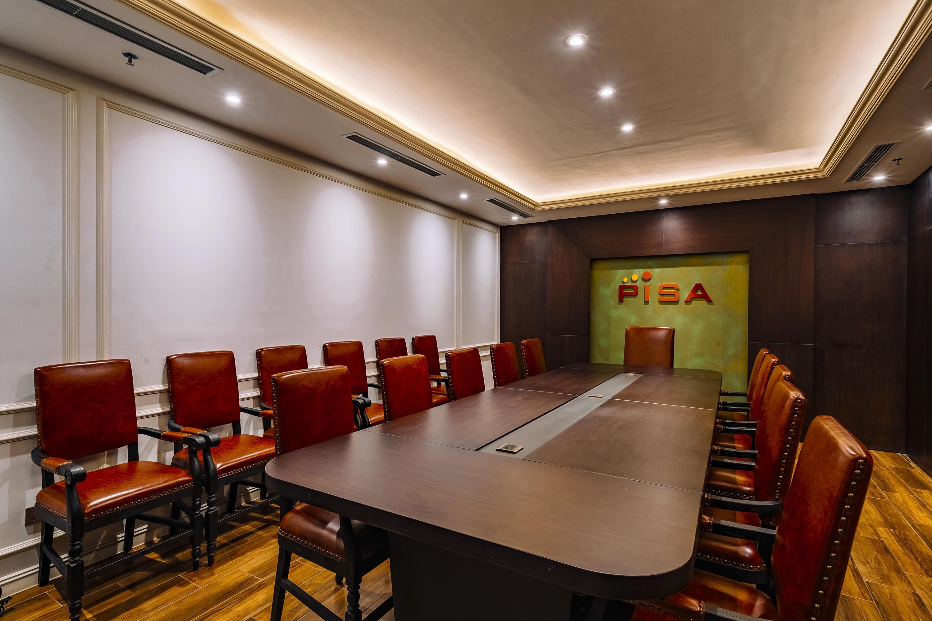 Ein Konferenzraum mit langem Tisch und roten Ledersesseln, Holzboden und einer Wand mit dem Schild 'PISA'.