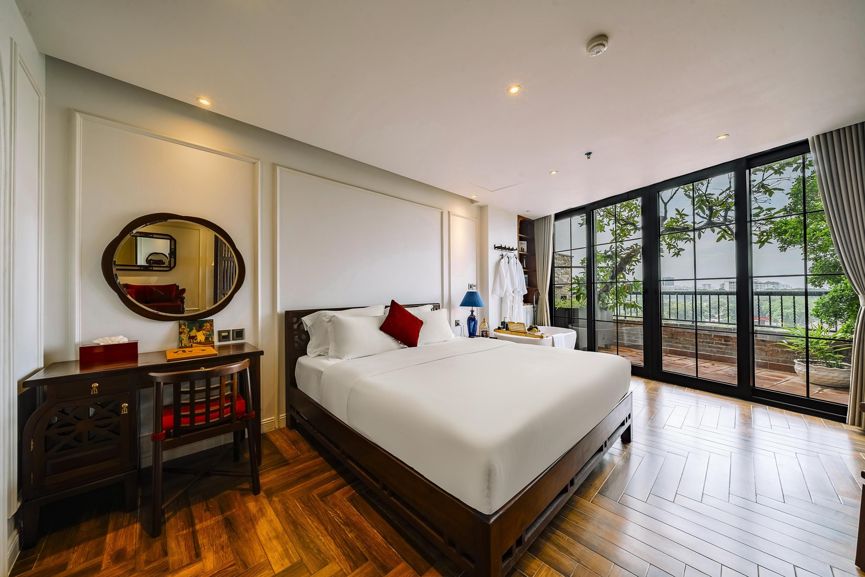 Habitación de hotel con una cama grande, una mesita de noche, un espejo y vistas al exterior a través de un ventanal.