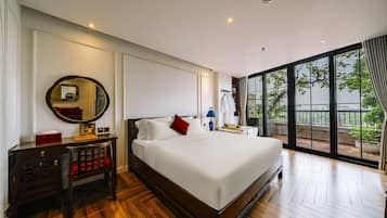 A hotel room with a large bed, a bedside table, a mirror, and a view of the outdoors through a large window.