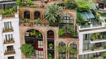 A multi-story building with a mix of traditional and modern architectural styles, featuring balconies, arched windows, and lush greenery.