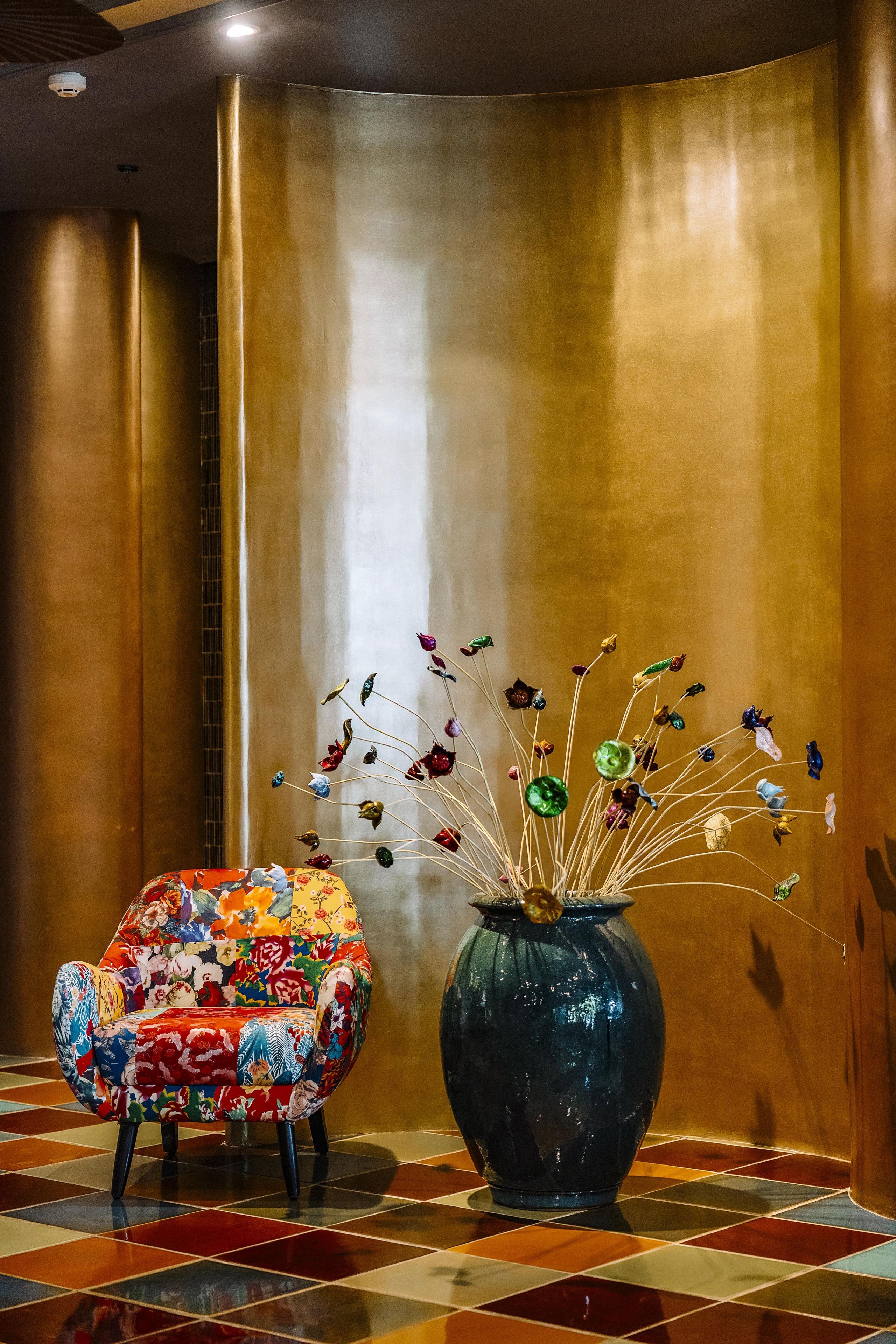 Ein Zimmer mit einer großen Metallwand, einem gemusterten Sessel und einer Vase mit bunten Blumen.