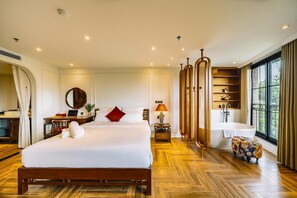 Ein Hotelzimmer mit einem großen Bett, einem Schreibtisch, einem Spiegel, einem Schminktisch mit Badewanne und einem Fenster mit Aussicht.