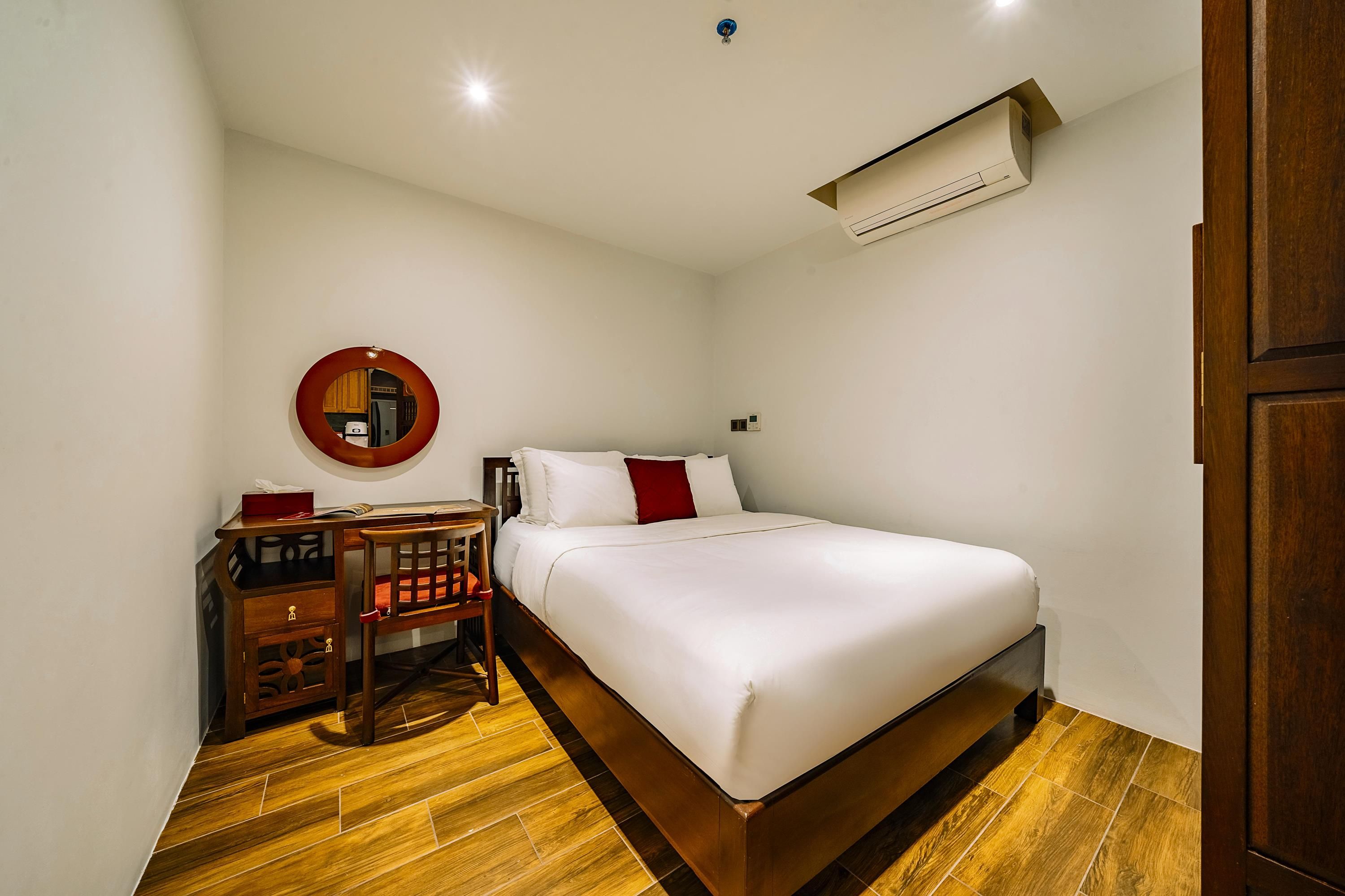 A bedroom with a bed, a desk, a chair, and an air conditioning unit.