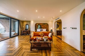 Un salón amplio con piso de madera en patrón espiga, un sofá, una mesa de centro con objetos decorativos y un ventanal con vistas a la ciudad.