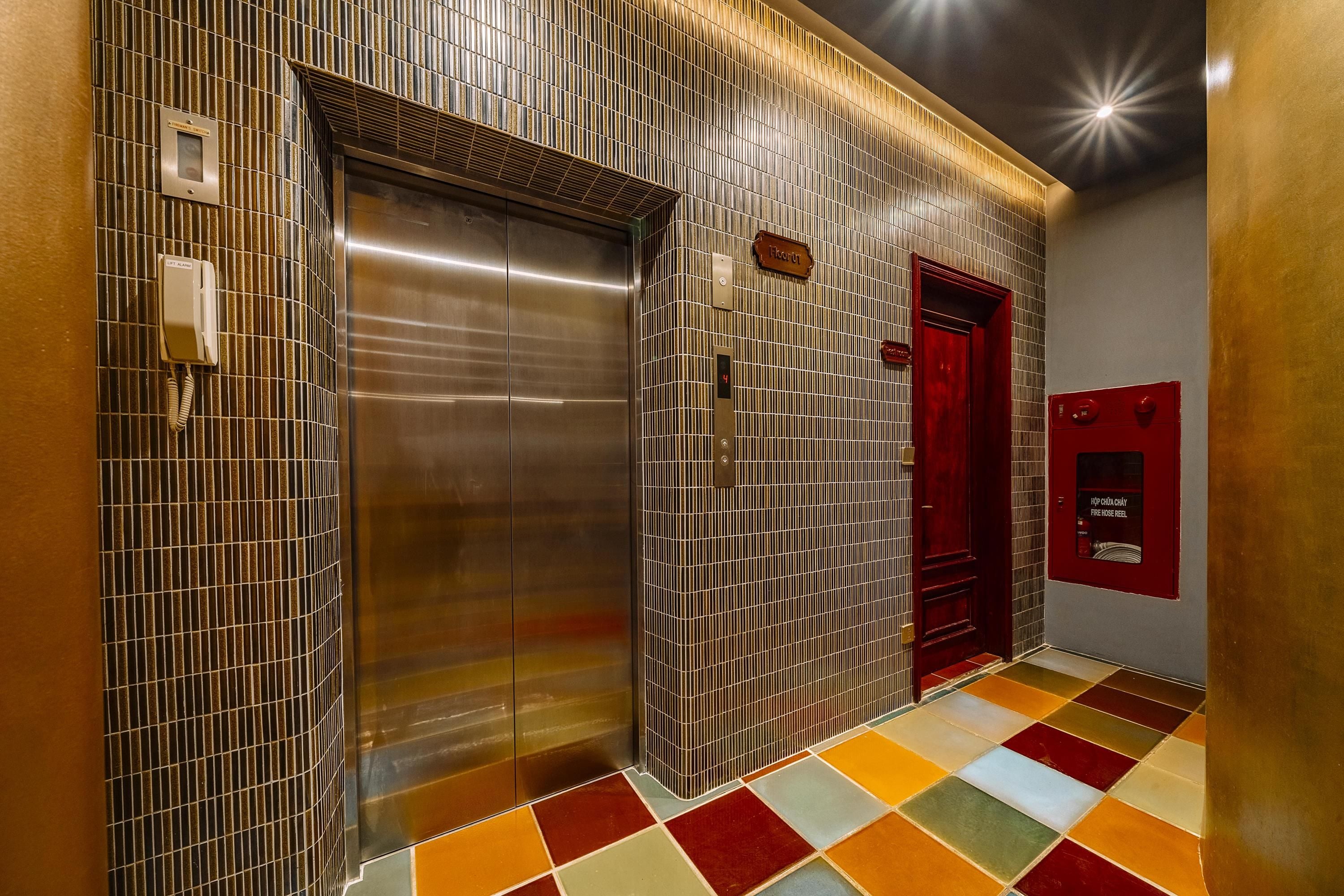 A modern elevator with a metallic finish, a red door, and a fire hose reel on the wall.