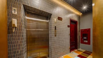 A modern elevator with a metallic finish, a red door, and a fire hose reel on the wall.