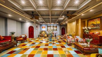 A hotel lobby with a checkered floor, red sofas, a chandelier, and ceiling fans.