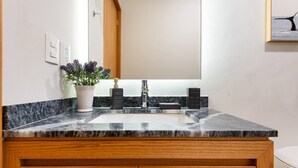 Une salle de bain avec un lavabo en marbre, des meubles en bois, une plante en pot et un miroir.
