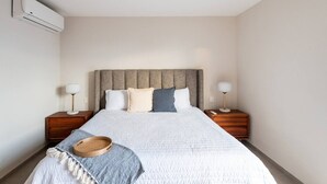 Une chambre à coucher comprenant un lit, deux tables de chevet, une commode, un climatiseur fixé au mur et une lampe de chevet.