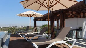 Une terrasse sur le toit, dotée de chaises longues et de parasols, une piscine et une vue sur la ville.