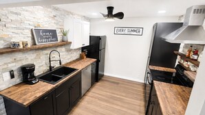 Una cucina moderna con zoccolo in pietra, mobili neri, piano di lavoro in legno e frigorifero nero, con un cartello che recita 'EVERY SUMMER HAS A STORY'.