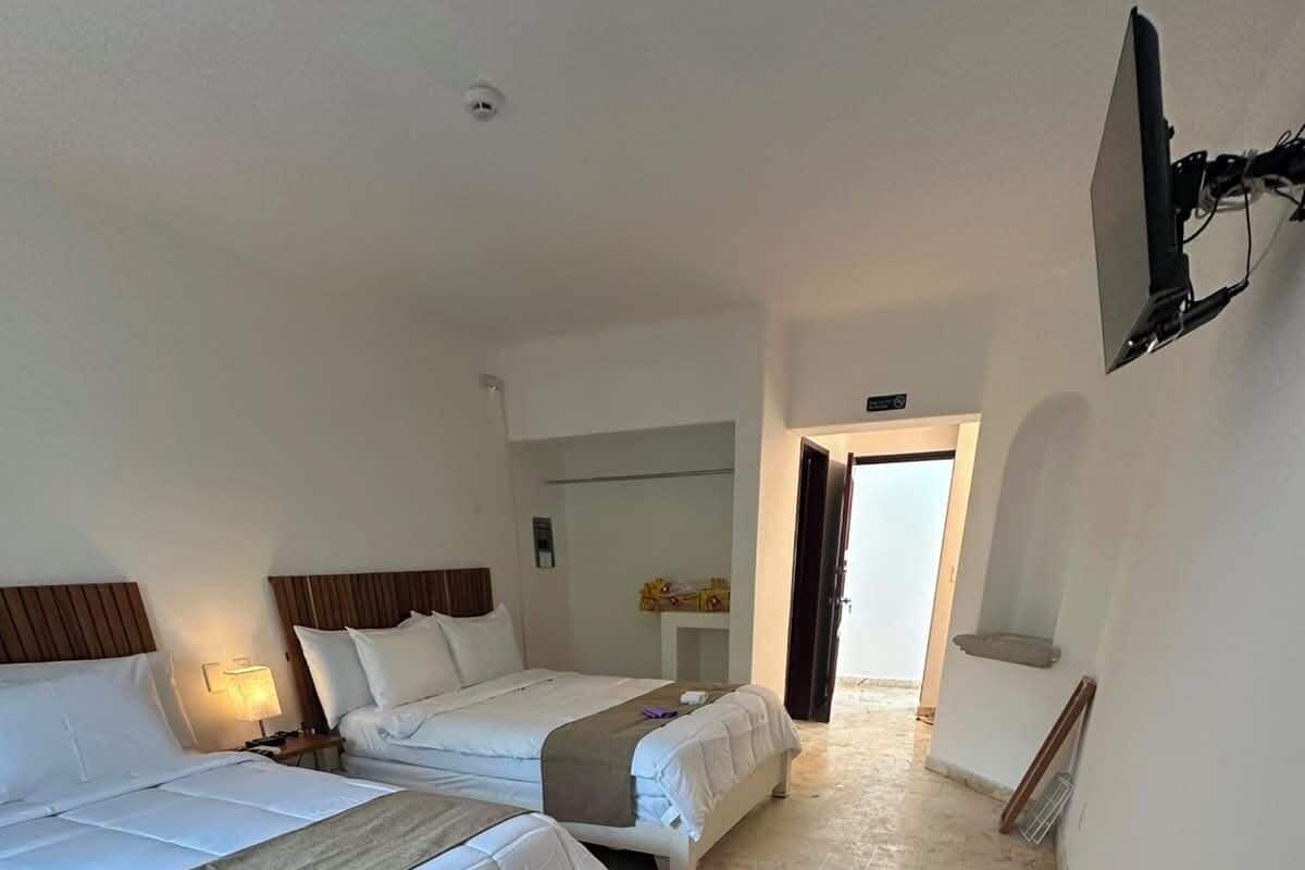 Habitación de hotel con dos camas, una mesita, una silla y un televisor montado en la pared.