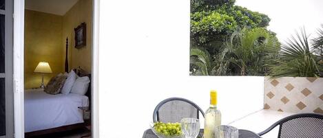 A room with a bed, a table with a bottle and glasses, and a framed picture on the wall.