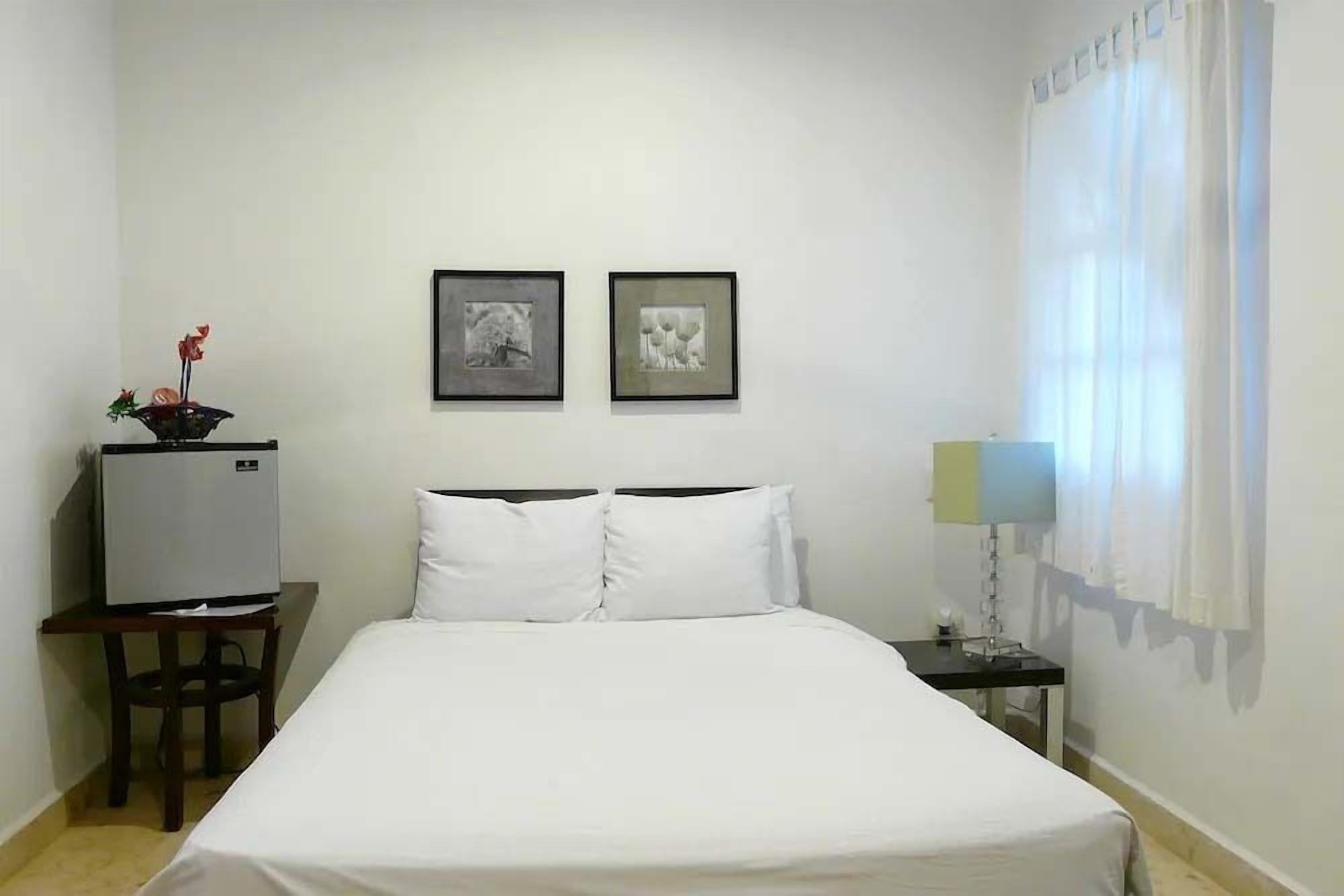 A hotel room with a bed, a desk with a television, and two framed pictures on the wall.