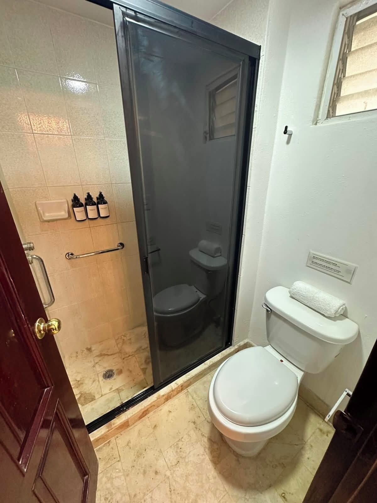 Ein kleines Badezimmer mit Toilette, Duschkabine und Waschbecken mit Seifenspendern.
