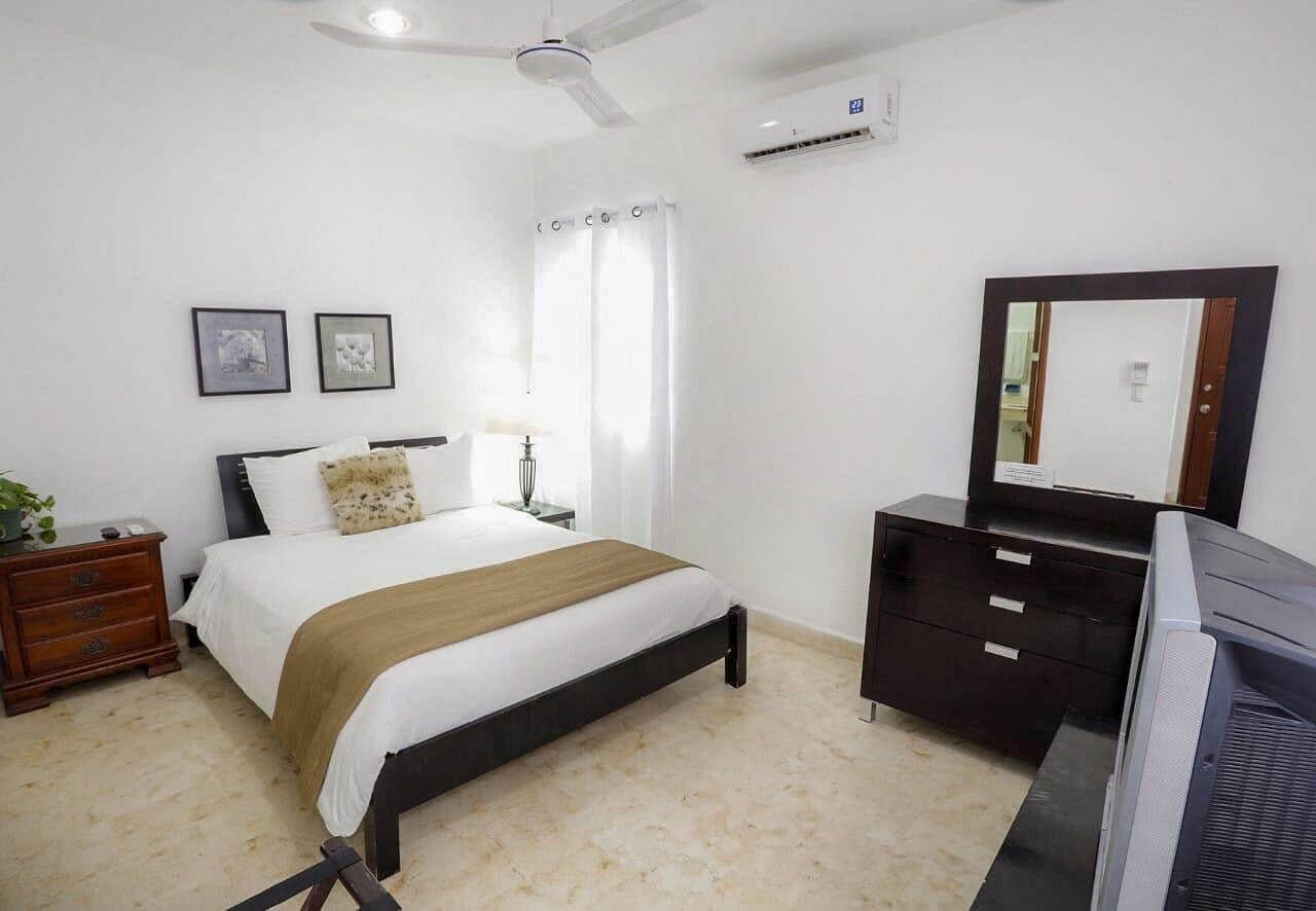 A bedroom with a bed, a dresser, a mirror, a ceiling fan, and an air conditioning unit.