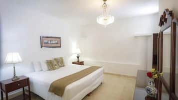 A hotel room with a bed, bedside lamps, a chandelier, a mirror, and a vase with flowers.