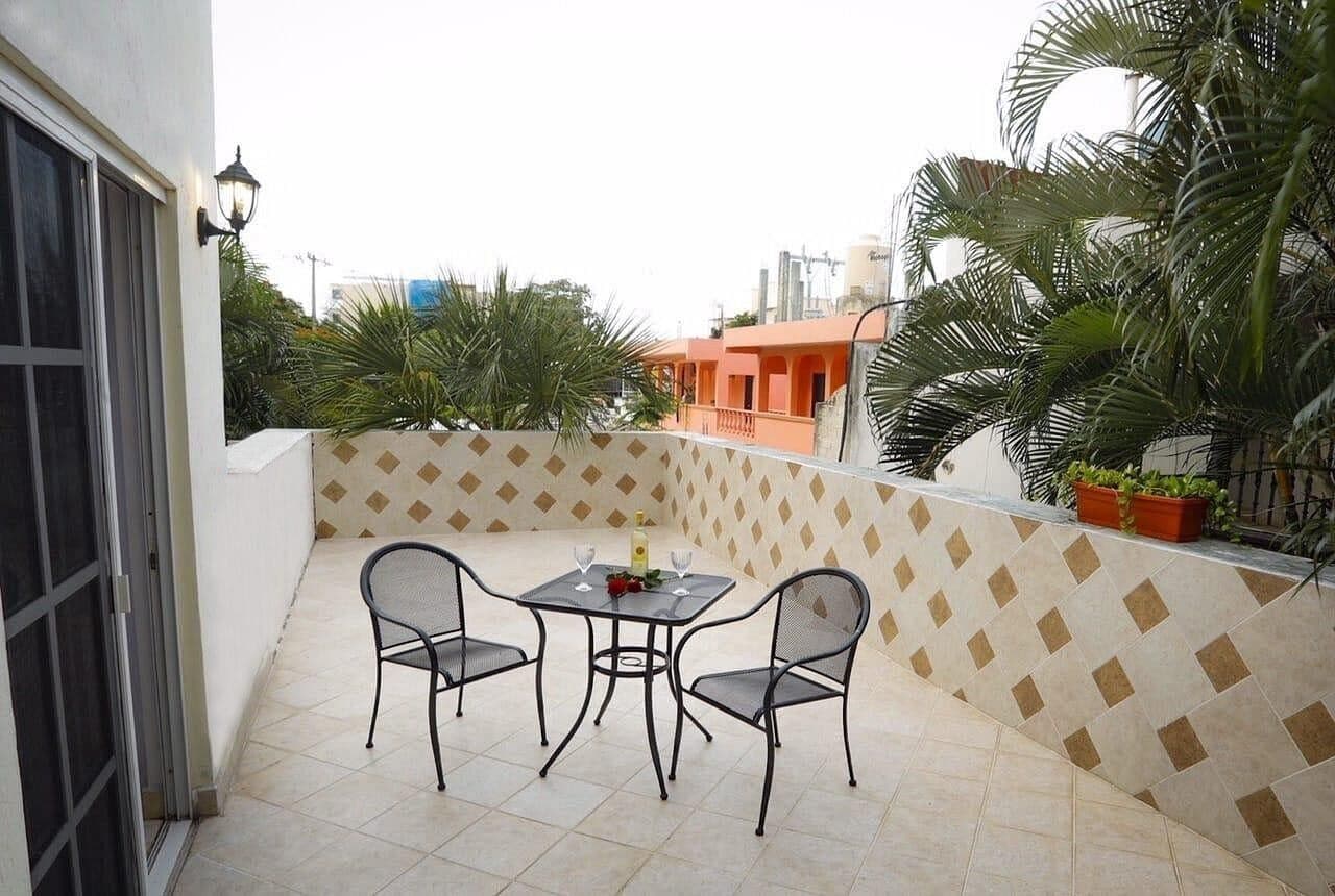 Een balkon met een tafel, stoelen, een betegelde vloer en een patroon op de muur.