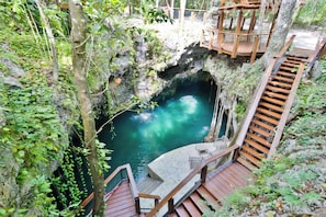 A wooden deck with stairs leading to a cave entrance, surrounded by greenery. - Luxury Jungle Villa - 4 Bedrooms - Private Pool and Cenote in a gated community (Puerto Morelos)