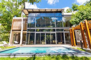 A modern house with a glass facade, a swimming pool, and outdoor seating. - Luxury Jungle Villa - 4 Bedrooms - Private Pool and Cenote in a gated community (Puerto Morelos)