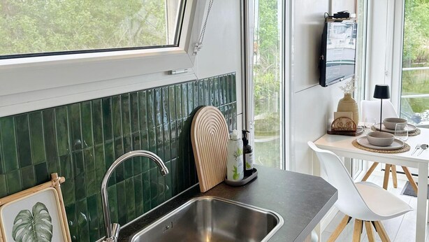 Una cocina con un lavabo, una ventana y un comedor con mesa y sillas.