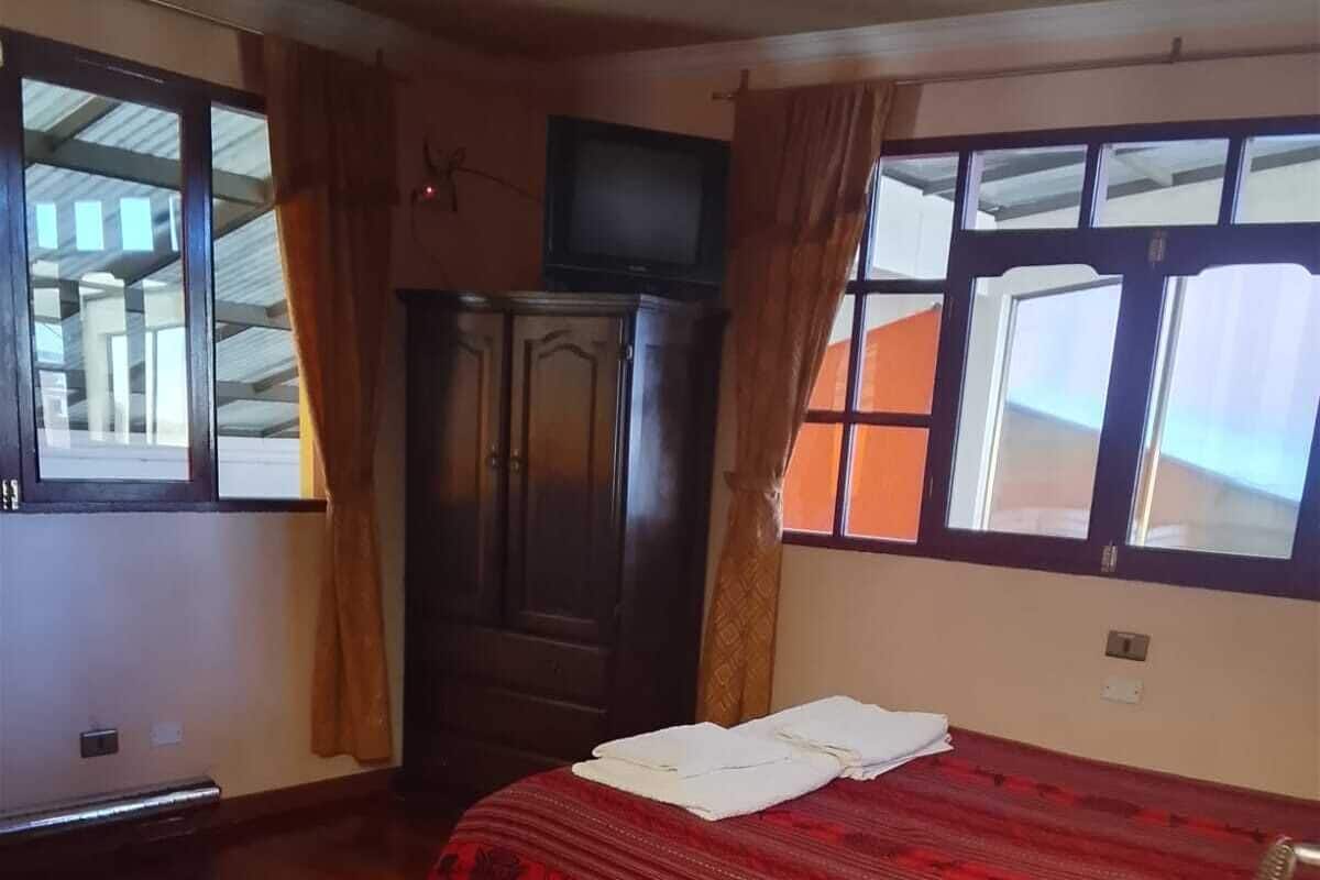 A room with a bed, a wooden desk, a wardrobe, and a television.