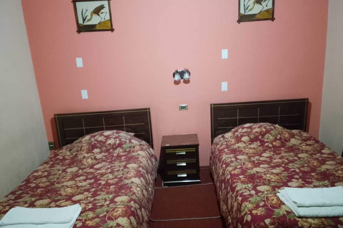 A room with two beds, a small table, and a wall-mounted light fixture.