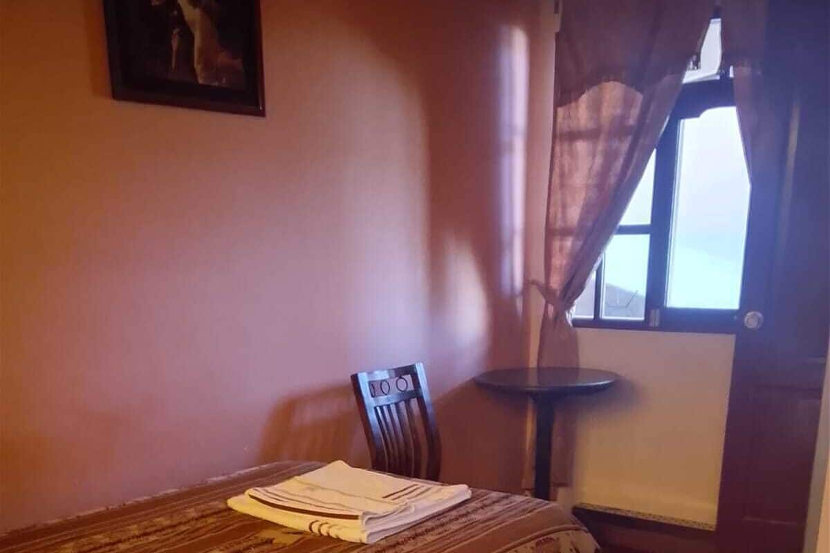 A small room with a bed, a chair, a small table, and a window with curtains.