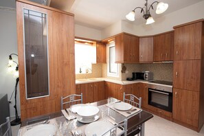 A kitchen with wooden cabinets, a dining table set for four, a microwave, and an oven. - Nikorina Apts | 4 (Apolpena)