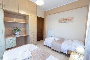 A bedroom with two beds, a dresser, a radiator, and a wall-mounted artwork. - Nikorina Apts | 4 (Apolpena)