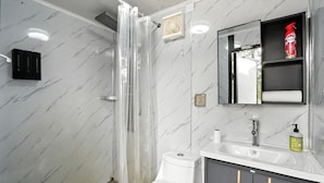 A bathroom with a shower, toilet, sink, and a mirror with a shelf above it.