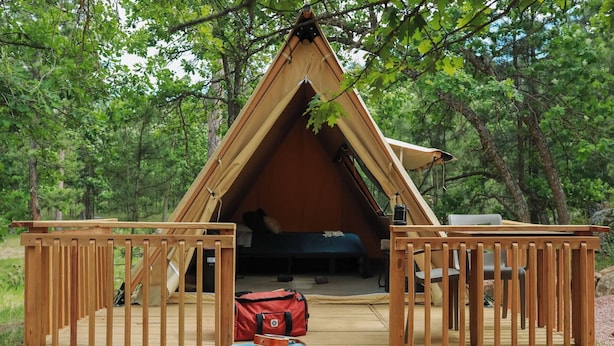 A tent with a wooden deck, a bed, and a red bag on the deck.