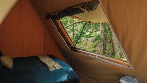 A tent with a bed, a window, and a view of trees.