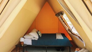 Une tente équipée d’un lit, d’oreillers, d’une lampe et d’une couverture.