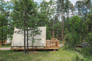 A glitzcamp with a covered sleeping area, wooden deck, and surrounding forest.