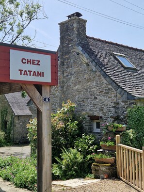 Un bâtiment en pierre avec une cheminée, une enseigne en bois sur laquelle on peut lire « Chez Tatani », et une petite fenêtre.