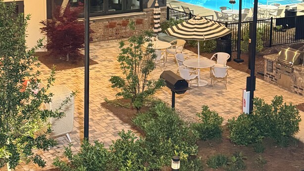 A pool area with lounge chairs, a barbecue grill, and string lights.
