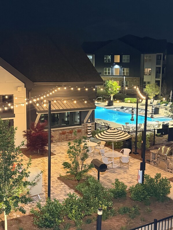 An outdoor pool area with lounge chairs, a barbecue grill, and string lights.