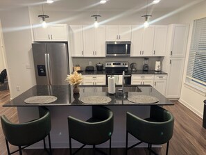 A modern kitchen with white cabinets, a central island with stools, stainless steel appliances, and pendant lighting.