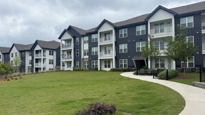 A multi-story residential building with balconies, a grassy courtyard, and outdoor seating.
