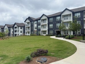 A multi-story residential building with balconies, a grassy courtyard, and outdoor seating.