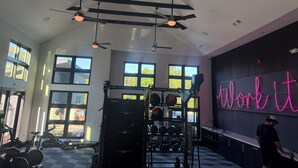 A gym with ceiling fans, exercise equipment, and large windows.