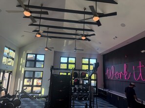 A gym with ceiling fans, exercise equipment, and large windows.