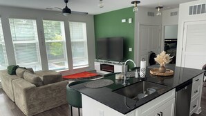 A modern kitchen with a central island, a dining area with a sofa, and a TV in the background.