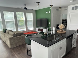 A modern kitchen with a central island, a dining area with a sofa, and a TV in the background.