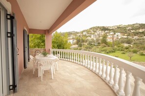 Ein Balkon mit geschwungener weißer Brüstung, einem Tisch mit Stühlen und Blick auf eine hügelige Stadt.