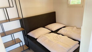 Una habitación pequeña y compacta con una cama, una estantería de madera y un ventanal.