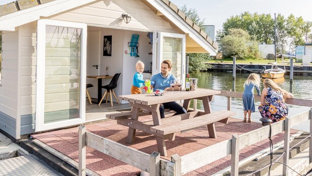 Una casa pequeña de un piso con un porche cubierto, una mesa de comedor y vista a un cuerpo de agua.