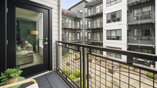 Un moderno edificio de apartamentos con varios balcones, entrada por puerta de vidrio y una pequeña zona de estar al aire libre.